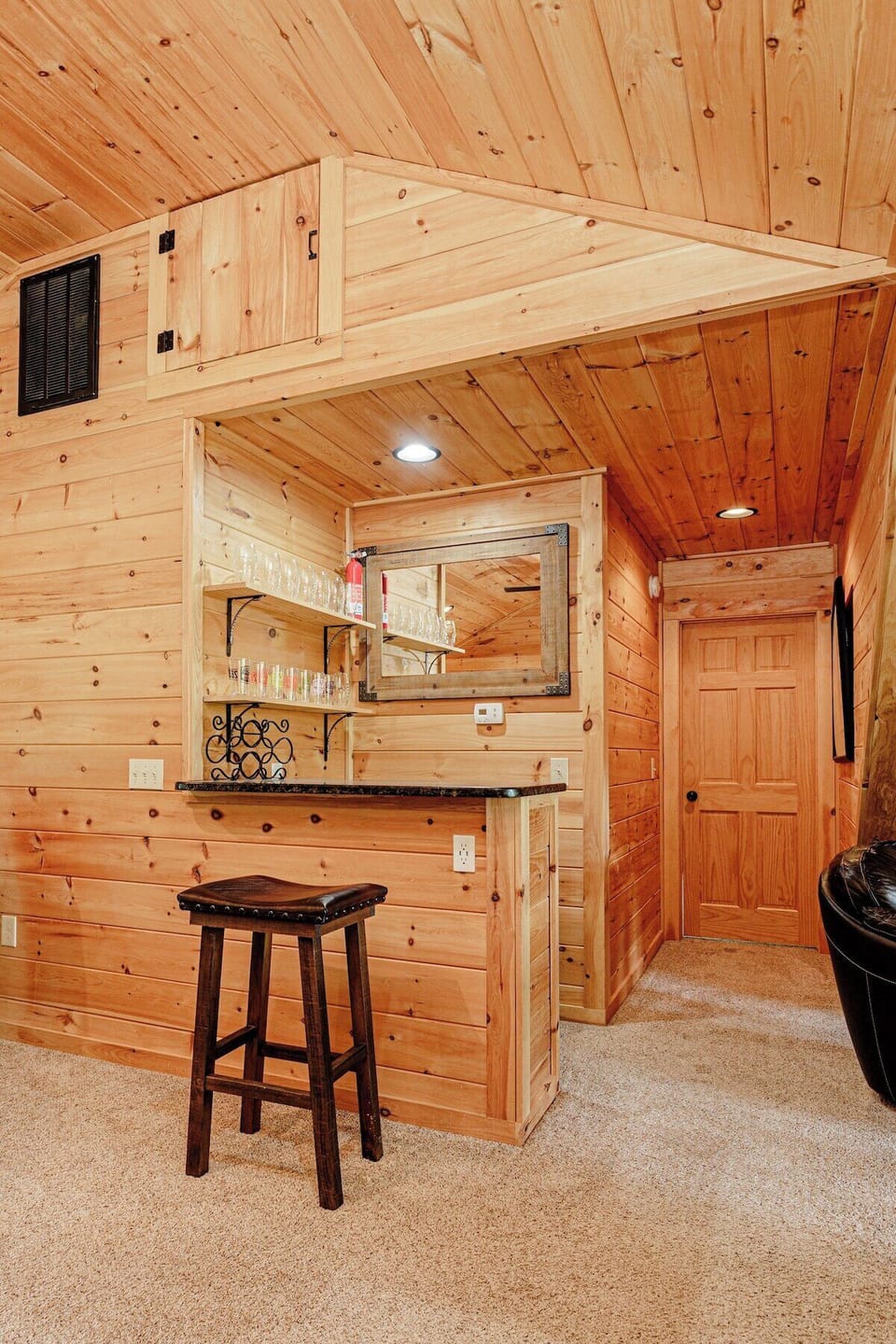 Basement wet bar with wood paneling, mirror backsplash, and seating for casual entertaining.