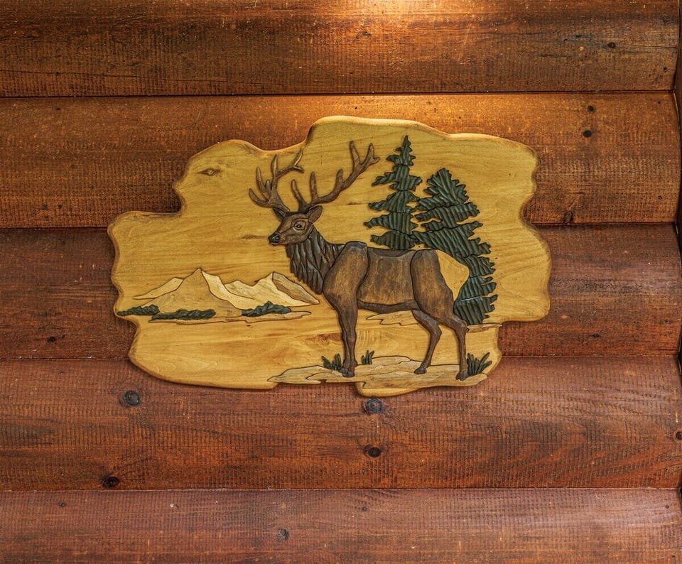 Decorative elk-themed wood wall art mounted on the log cabin exterior at Elk Crossing. Rustic cabin details reflect the mountain lodge atmosphere of this Bryson City retreat.