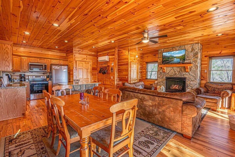 Open-concept living room and dining area with a hand-crafted stone fireplace, leather seating, and full kitchen inside this Bryson City cabin near the Great Smoky Mountain Railroad and Lake Fontana.