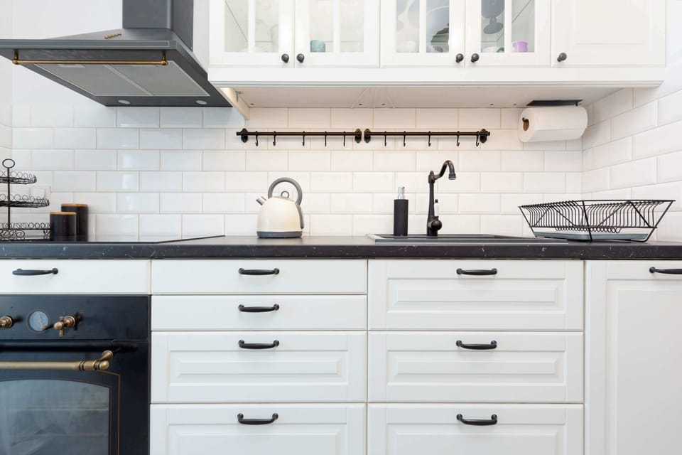 A modern kitchen area with a white tiled backsplash, black countertop, and open shelving for a contemporary feel.