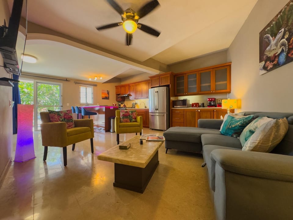 Living room with a gray sectional, floral-patterned armchairs, marble coffee table, and ceiling fan lighting.