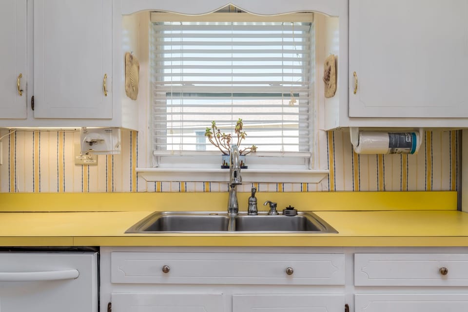 Your sunny kitchen features cheerful yellow countertops and charming vintage touches, perfect for preparing meals with natural light streaming through the window.
