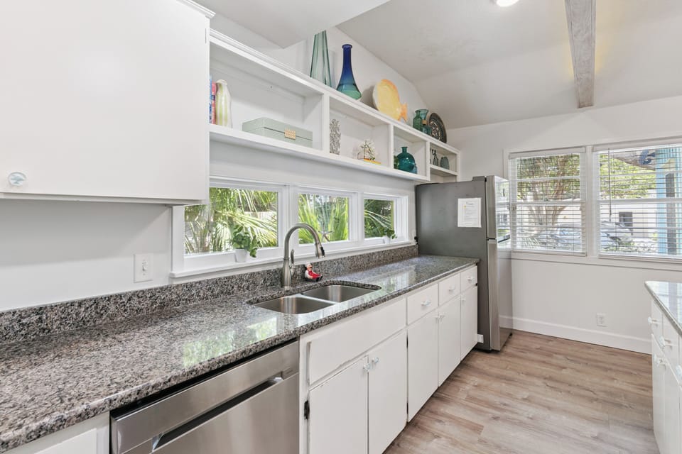 Your fully equipped kitchen awaits, where crisp white cabinetry meets sleek granite counters and tropical views through sunny windows invite effortless meal prep.