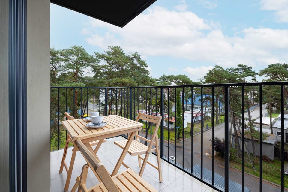 A balcony with a small table and two chairs, perfect for relaxing and enjoying a view of the forested area in the background.