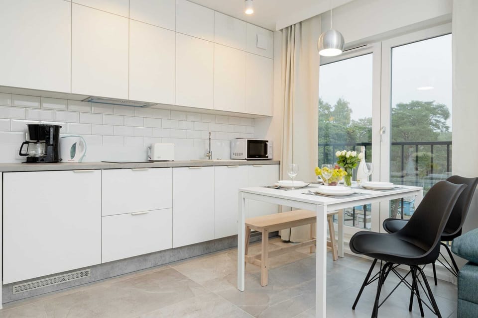 A minimalist kitchen with white cabinetry and a dining table positioned nearby, creating a functional and open cooking and dining space.