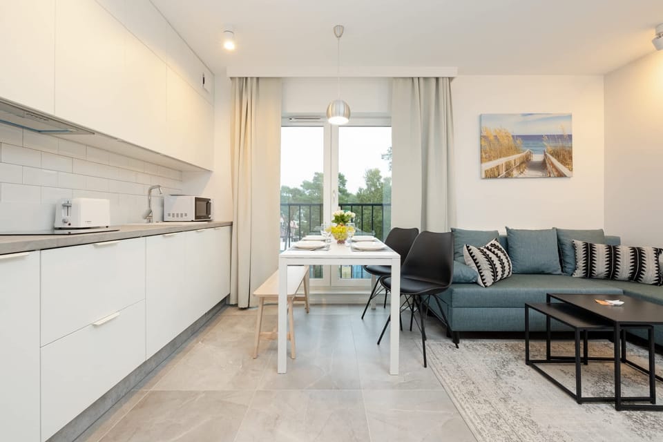 A bright, open-plan space combining a modern kitchenette with sleek white cabinets and a cozy living area. The layout is functional, allowing seamless transition between cooking and relaxation.