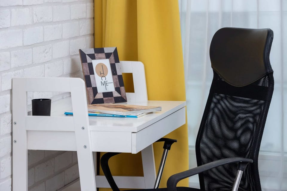 A functional workspace with a comfortable black ergonomic chair and a white desk.

