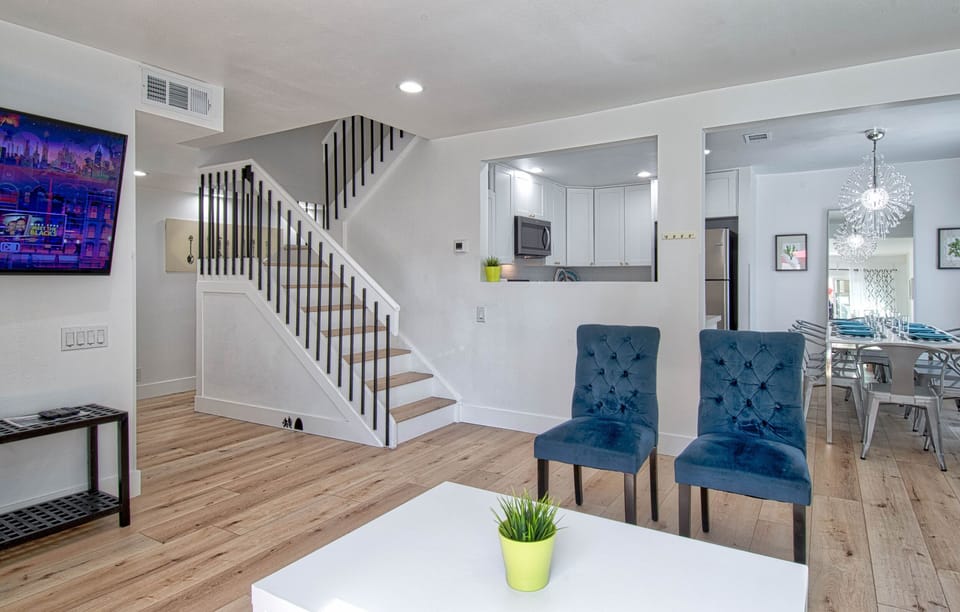 - Bright open living area with cozy seating and clean design layout   - White walls and natural wood flooring create a warm atmosphere   - Spacious spot to relax with direct access to the kitchen area