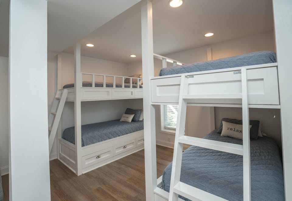 Bonus bunk area with built-in white bunk beds, blue bedding, ladders, storage drawers, recessed lights, gray sectional edge, and wood-look floors.