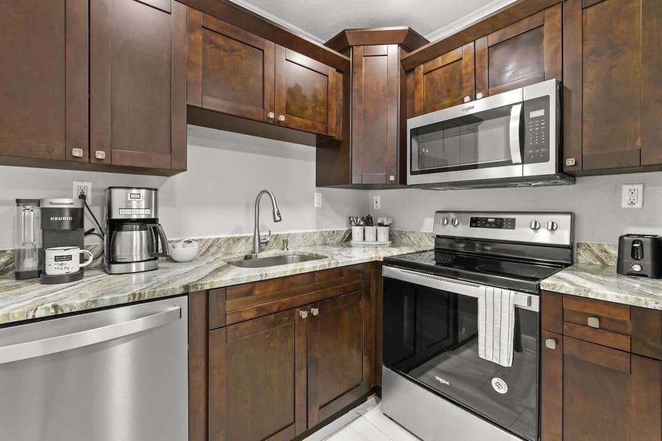 The kitchen features classic dark cabinets and stainless steel appliances, including a spacious refrigerator, oven, stovetop, and dishwasher. It’s fully stocked with all the essentials and offers both Keurig and drip coffee makers for your convenienc