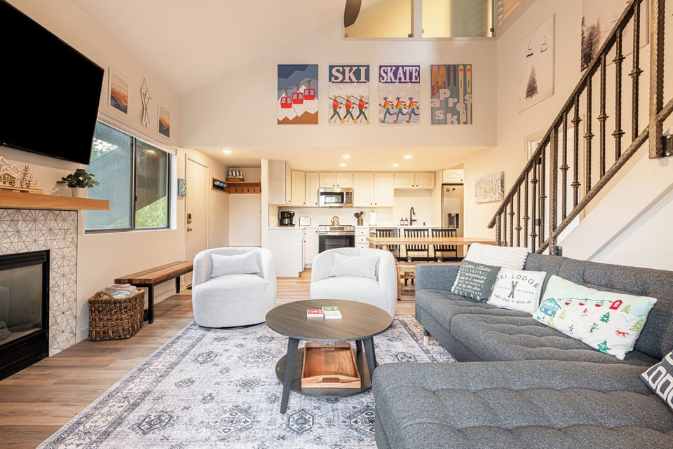 Bright, stylish living room with vaulted ceilings, cozy seating, and a large TV — perfect for relaxing after a ski day.