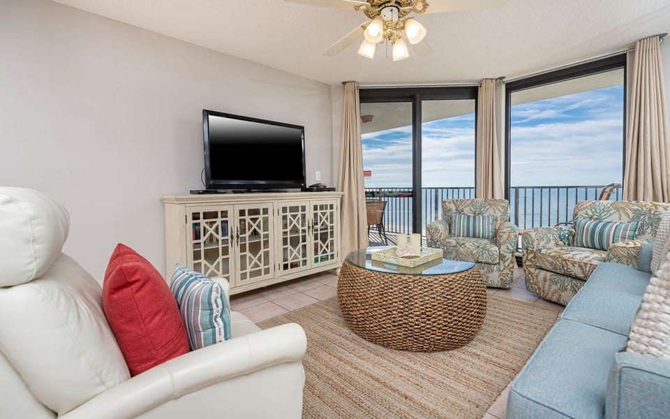 Cozy living area features a light blue sofa with queen sleeper, tropical-patterned chairs, and a view of the gulf
