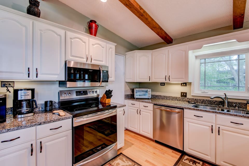 A fully equipped kitchen ready for mountain mornings, with granite counters, stainless appliances, and warm wood beams overhead.