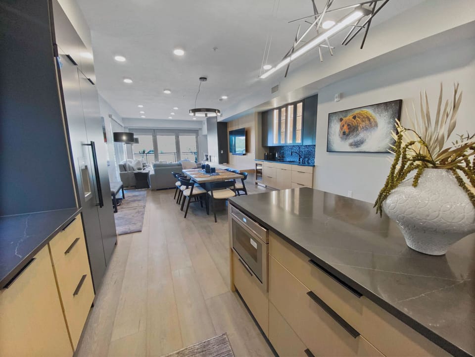Gather in our open-concept living space, featuring a modern kitchen island with bar seating, a large dining table, and two-tone cabinets. Perfect for memorable meals and relaxing.