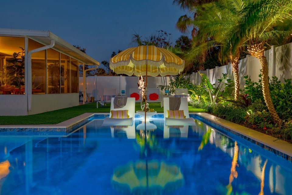 Private pool lit up at night with palms, ambient lighting, and a relaxed retro-coastal vibe.