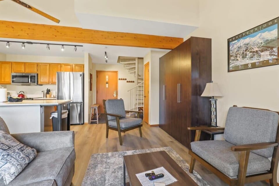 Another angle of the living room shows the armchair seating, full-size Murphy bed when tucked in as well as the kitchen, entrance and spiral staircase to the upstairs loft bedroom.