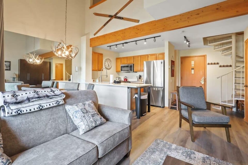 View of the open-concept family room, fully-equipped kitchen and dining room as well as the front door entrance and spiral staircase to the upstairs loft bedroom.