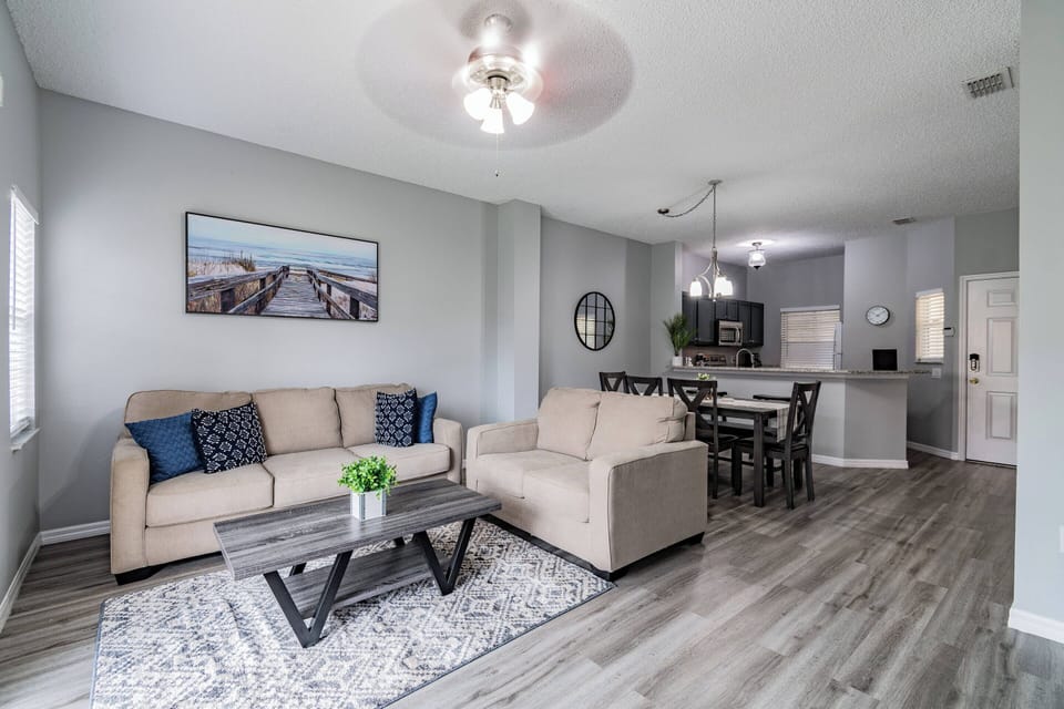 This bright living area features a cozy beige sofa with navy pillows and a stylish coffee table on a soft rug, effortlessly connecting to a modern dining space for an inviting atmosphere perfect for relaxation and gatherings.
