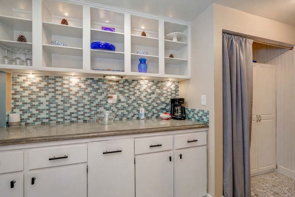 Bright and functional kitchenette featuring elegant tile backsplash, open shelving, and a coffee station.