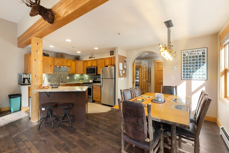 A kitchen and dining area featuring wooden accents, an island with stools, stainless steel appliances, and a dining table with six chairs. A Colorado-themed poster is on the wall.