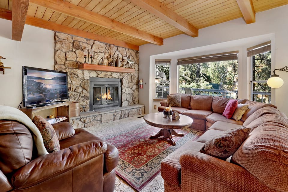 Cozy mountain living room with a stone fireplace, comfy seating, and smart TV—perfect for relaxing evenings, movie nights, and warm cabin vibes after outdoor adventures.