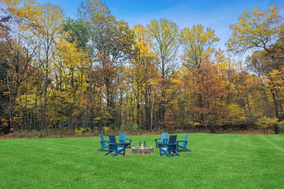 Fire pit seating overlooks a spacious lawn framed by brilliant fall foliage.