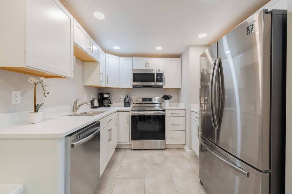 - Fully equipped kitchen with white cabinetry, stainless appliances, and sleek countertops
- Compact layout includes a full size fridge, microwave, dishwasher, and coffee essentials
- Neutral palette and tile floors make cleanup quick and easy