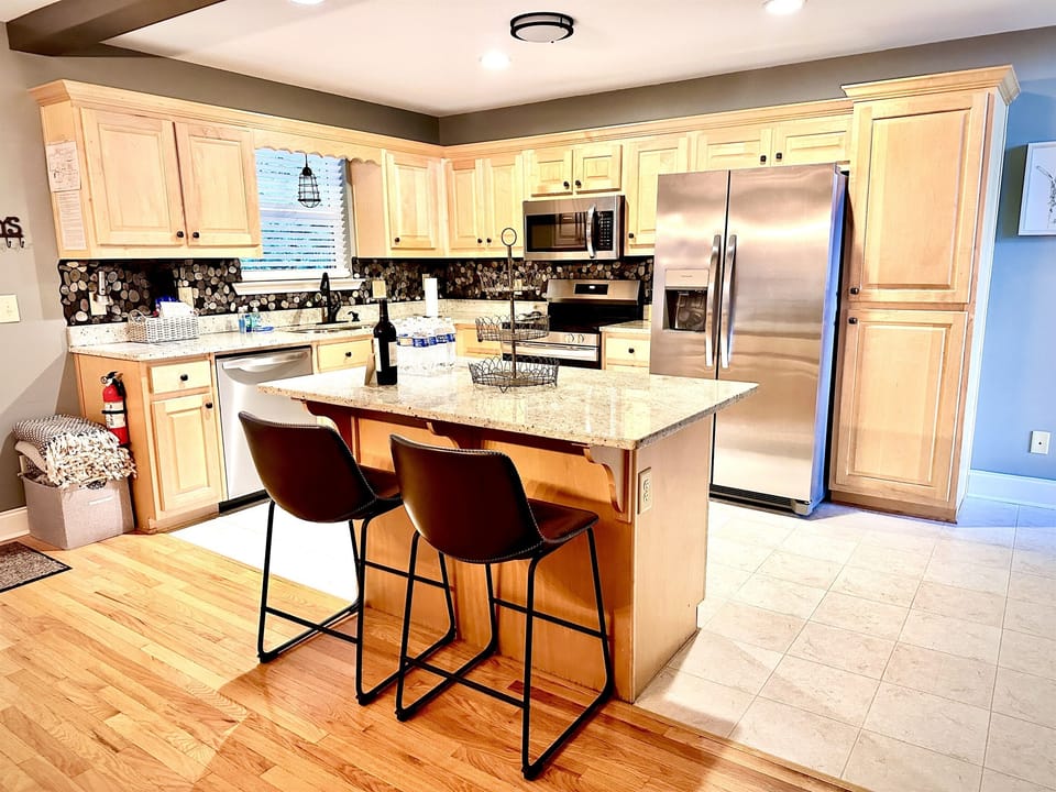 Step into a modern kitchen with stainless steel appliances, a spacious island, farmhouse table, coffee bar, and fully stocked cookware—perfect for gathering, cooking, and enjoyi 