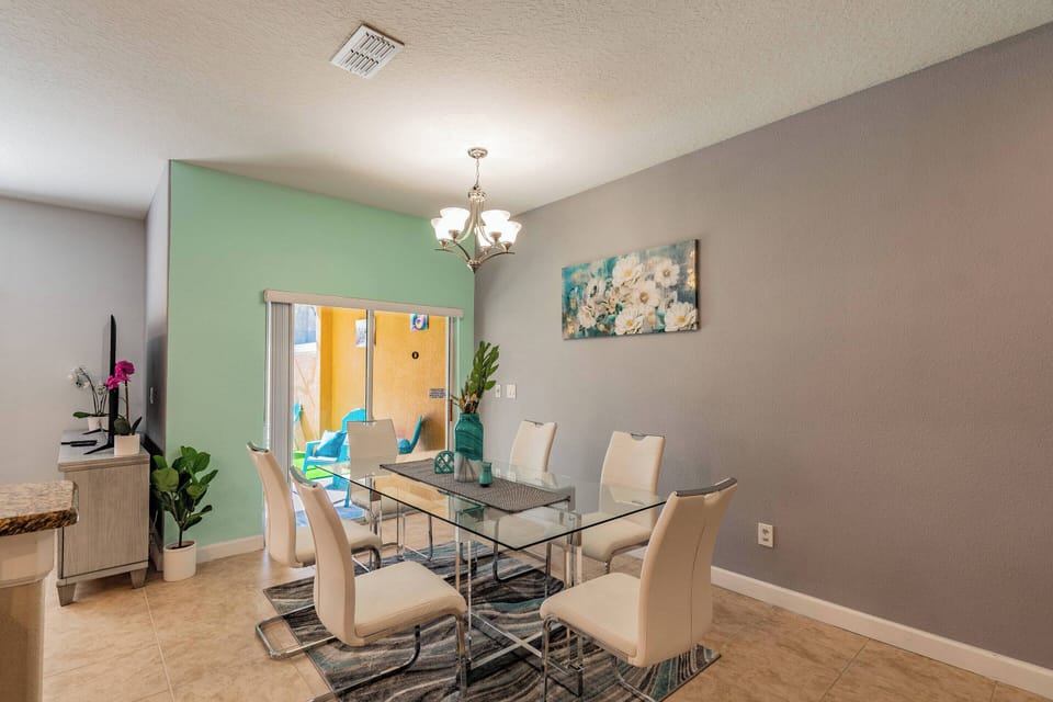 Enjoy shared meals in this bright dining area featuring a sleek glass table and six plush white chairs. The soft green accent wall and charming artwork, combined with natural light from the sliding doors, create a warm atmosphere.