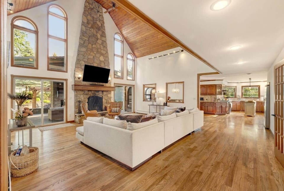 Relax in the elegant living room featuring a vaulted ceiling, grand stone fireplace, and cozy seating. Warm and inviting, it's the perfect space to unwind, connect, and enjoy the morning and evening passing of deer alongside the property.