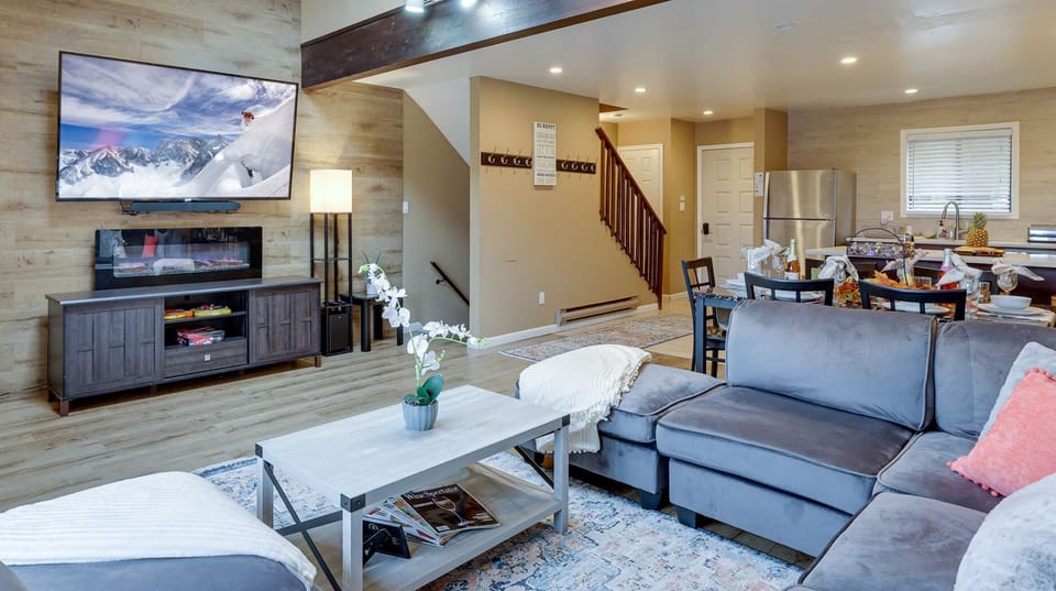 Living room featuring a 75 inch smart TV with Netflix and Roku. Connects to Balcony with mountain view blue sky and trees. Board games for family, comfortable couch, ample lighting.