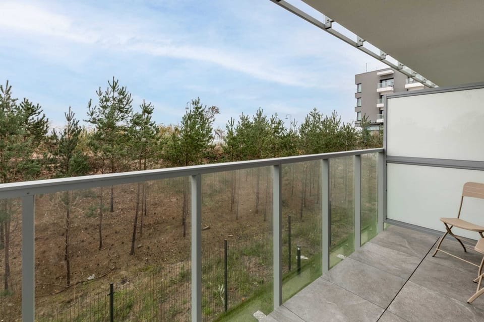 A private balcony with glass railings offering views of a peaceful forest and greenery.
