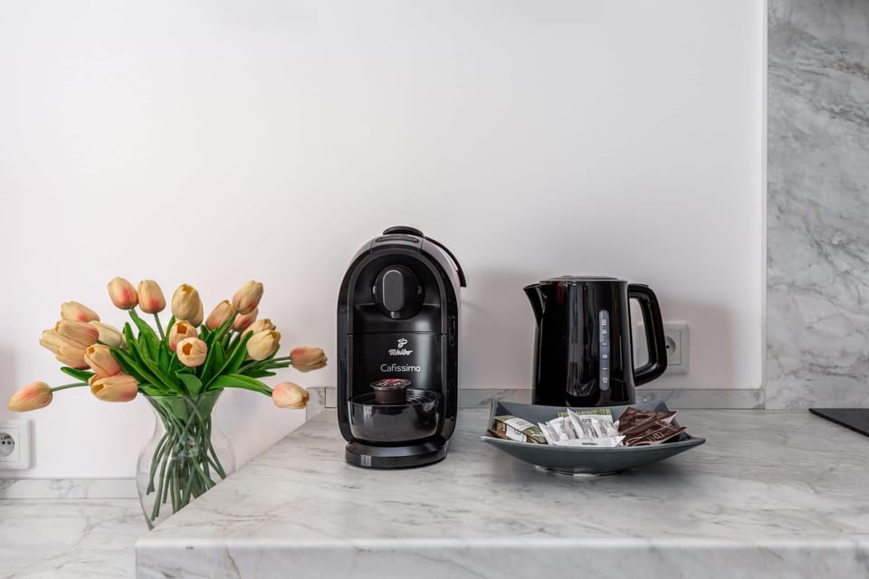 A compact kitchen corner with a coffee maker, kettle, and fresh tulips adding a vibrant touch.
