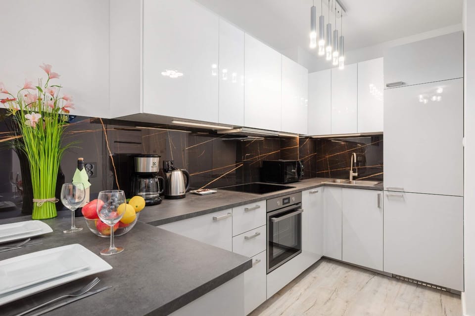 A sleek, fully equipped kitchen with white cabinets, a dark backsplash, and modern appliances.
