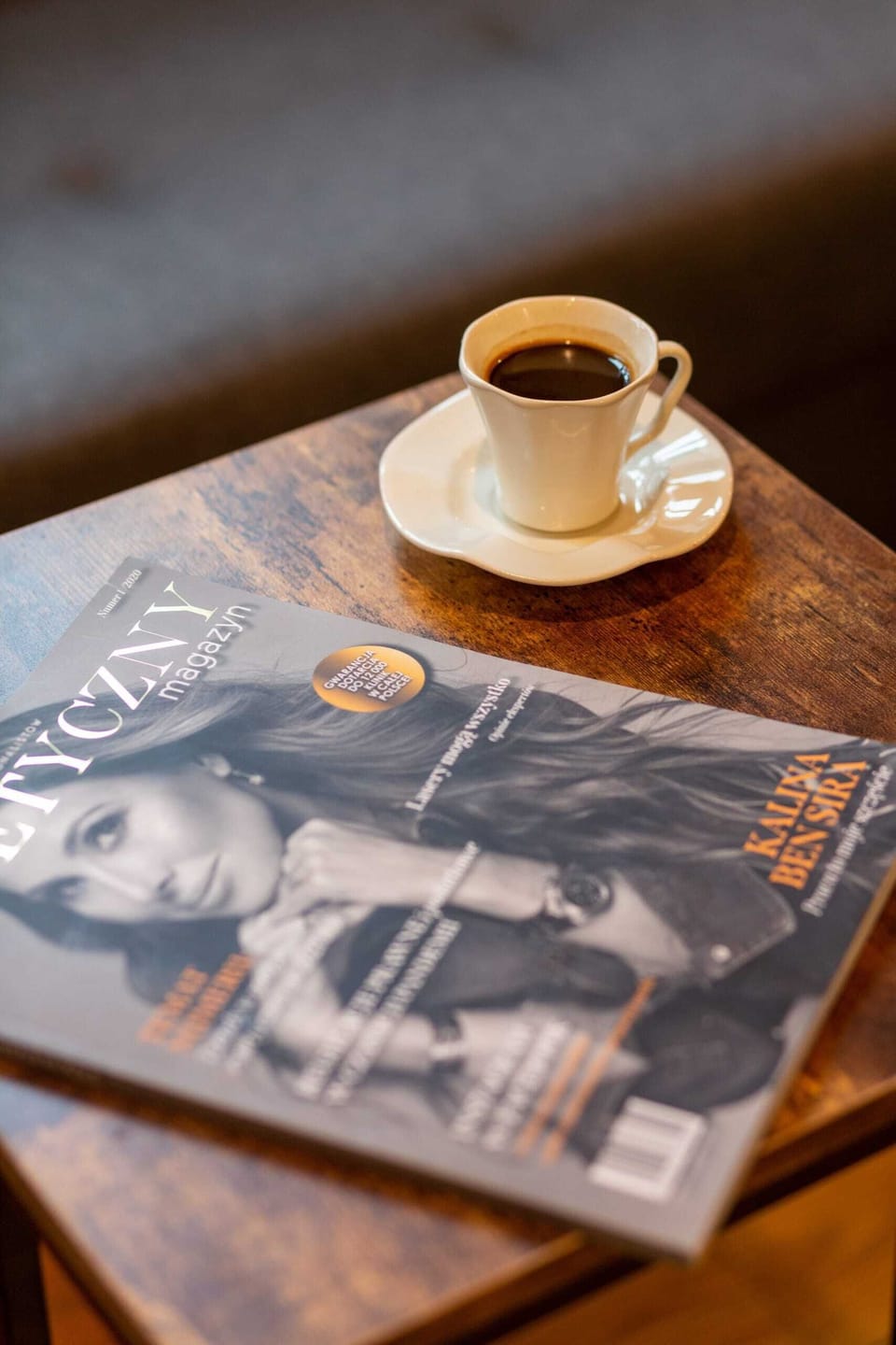 A cup of coffee served on a wooden table with a magazine, adding a cozy, home-like ambiance.
