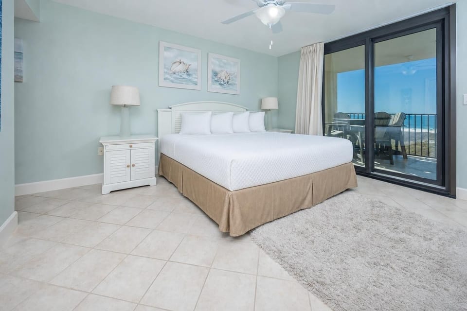Master bedroom featuring a king bed, soft rug, and sliding glass doors leading to a balcony with beach views