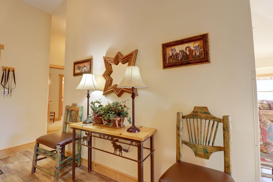 A cozy hallway featuring a wooden table with two lamps, green wooden chairs on either side, a mirror, and framed paintings on the wall.