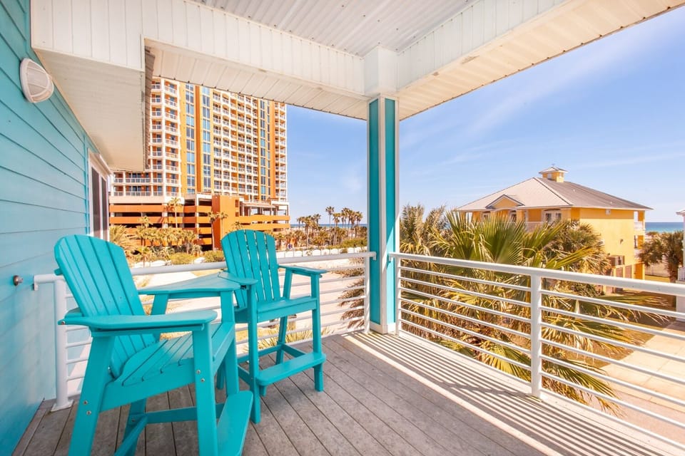 The primary bedroom features a private balcony with turquoise Adirondack chairs, partial Gulf views.