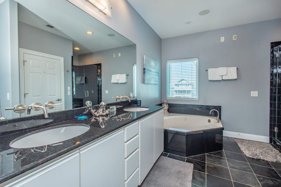 Your luxurious en-suite bathroom features dual sinks with sleek granite countertops, a deep soaking tub, and a separate glass-enclosed shower—a serene retreat after exploring the island.