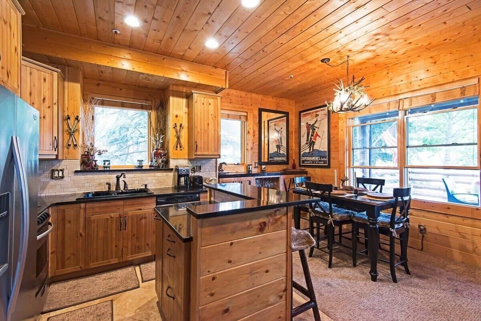 The lovely kitchen area boasts an island with bar seating for two, stainless steel appliances, wood finishes, a tile backsplash and nature views from the kitchen sink.