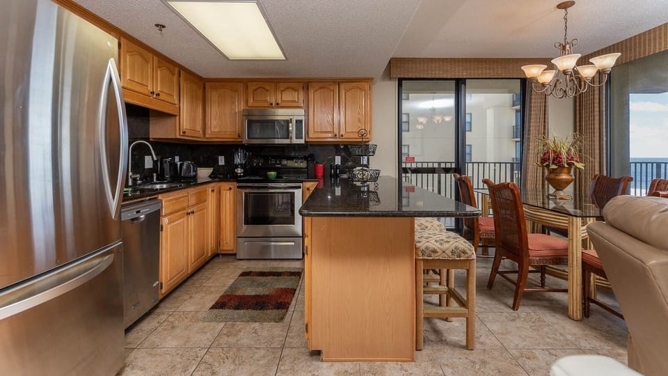 Modern kitchen features warm wood cabinetry, a breakfast bar with seating, and views of the gulf through large windows