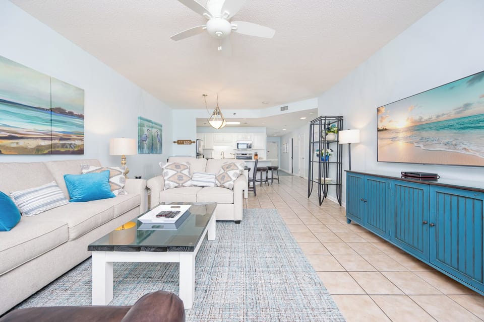 Light and airy living area features a comfortable sofa with queen sleeper, vibrant accents, and a large TV