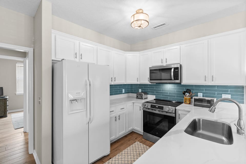 Your fully-equipped kitchen awaits with crisp white cabinetry, modern stainless appliances, and lovely teal backsplash accents—perfect for preparing meals and gathering together.