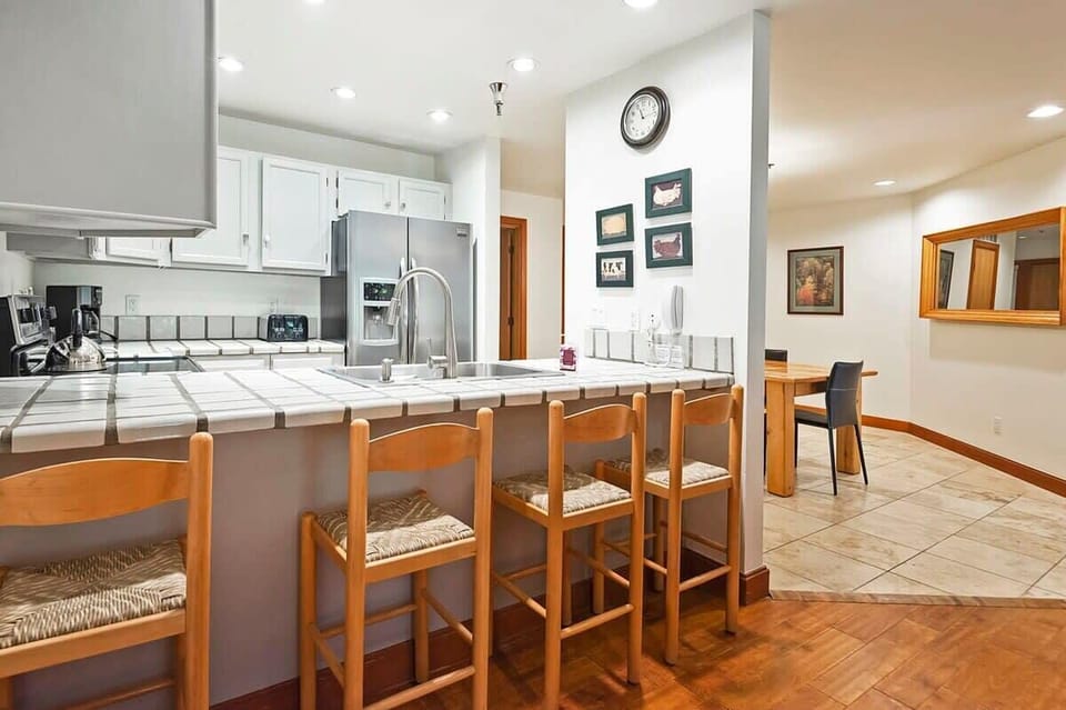 Fully-equipped kitchen with modern stainless steel appliances, tile countertop, and breakfast bar seating for 4