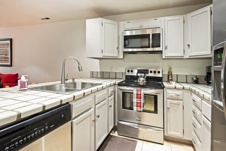Fully-equipped kitchen with modern stainless steel appliances, tile countertop, and breakfast bar seating for 4