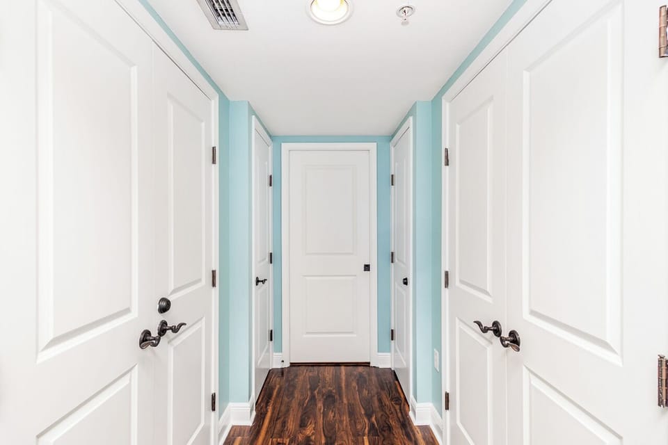 Step into your private hallway where soft blue walls and gleaming hardwood floors greet you, leading to your peaceful retreat spaces behind each door.