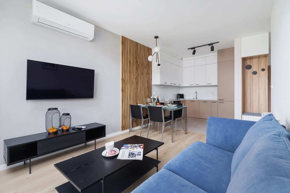A bright, air-conditioned living room space that is coherently connected by a dining table and kitchenette. A large flat-screen TV hangs on the wall which provides evening entertainment.