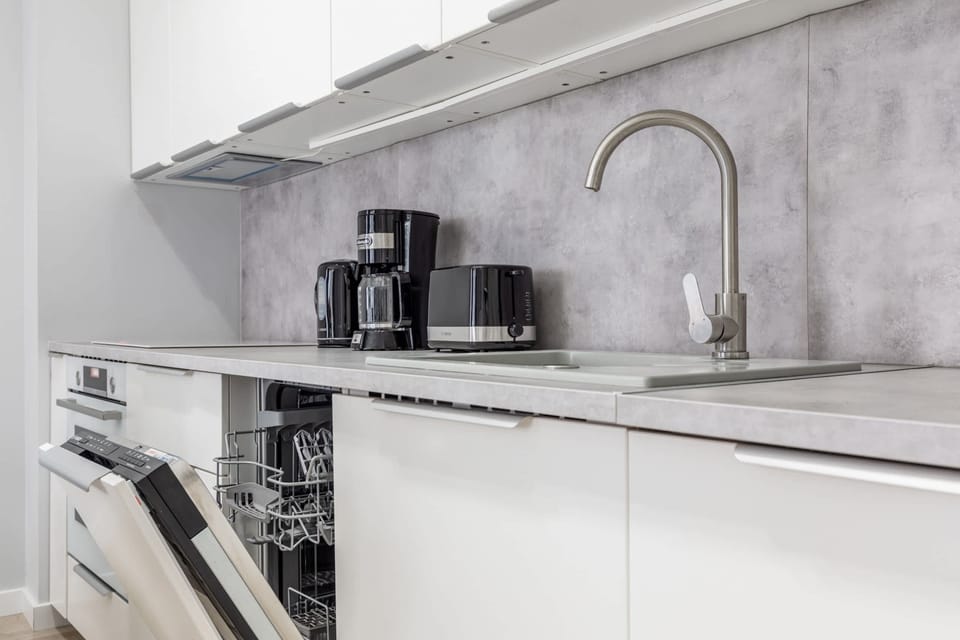 Close-up of the kitchenette with white cabinets and matching grey worktop. There is a dishwasher in the kitchen and a coffee machine and toaster on the countertop.