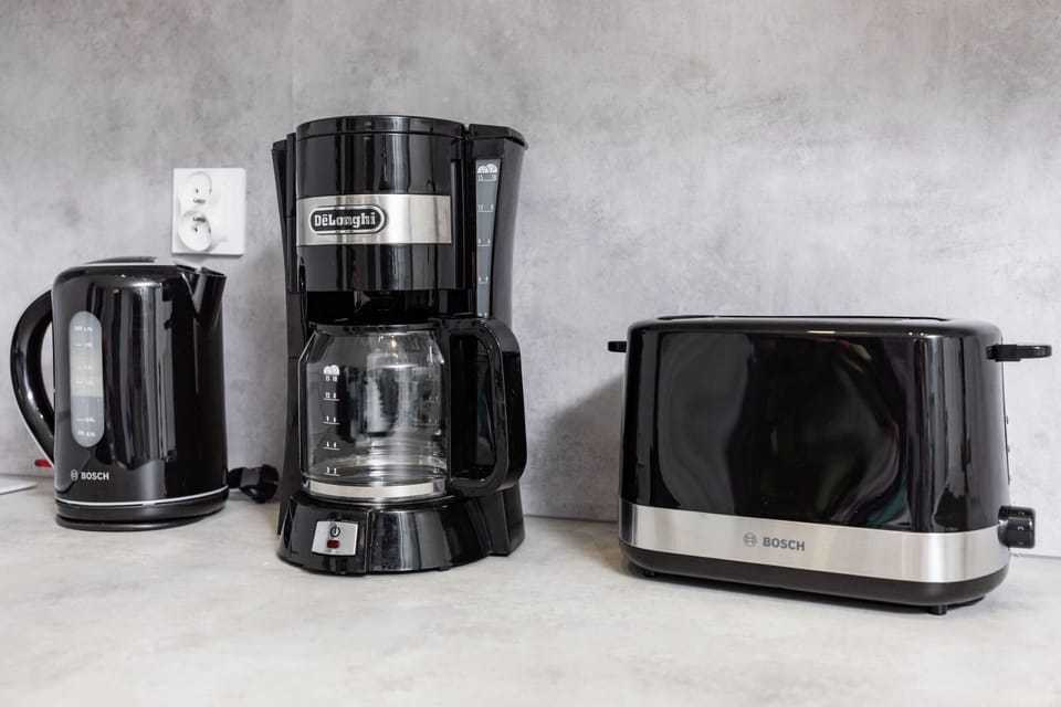 Glancing at the kitchen worktop on which stands a black electric kettle, coffee machine and toaster.