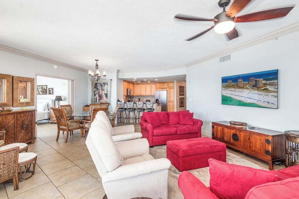 Settle into your spacious living room where bright coastal artwork and plush seating create an inviting retreat. Tile floors and ceiling fans keep you cool while the open layout flows seamlessly into the dining area and fully-equipped kitchen.